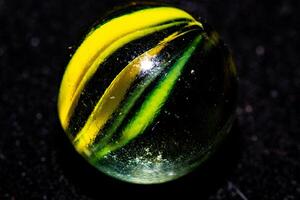 Close-up of a colorful glass marble with yellow and green swirls on a dark background. photo