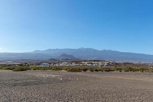 Panoramic view of a sandy beach with a mountain range in the background under a clear blue sky in Tenerife. photo