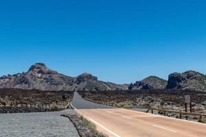 Desert road stretching into the distance with rocky mountains under a clear blue sky in Tenerife. photo