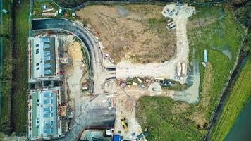 aéreo ver de un construcción sitio con excavado tierra, maquinaria, y materiales, rodeado por verdor. foto