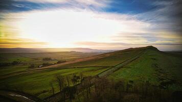 Scenic view of rolling hills at sunrise with vibrant sky and lush greenery, ideal for backgrounds or nature themes at Sycamore Gap, Northumberland, UK. photo