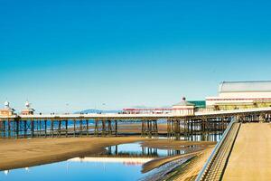 Serene seaside pier with clear blue sky reflected in calm water, showcasing tranquil coastal scenery in Blackpool, England. photo