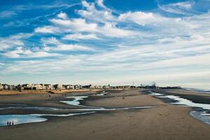 Serene beachscape with scattered pools of water, under a vast blue sky, with distant buildings lining the shore in Blackpool, England. photo