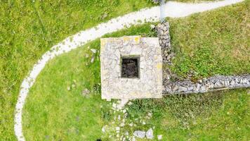 Aerial view of a small stone structure with a path in a green grassy field. photo