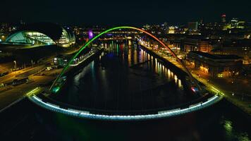 noche ver de un paisaje urbano con iluminado arqueado puente terminado un río, reflejando vistoso luces en agua en Newcastle sobre Tyne foto