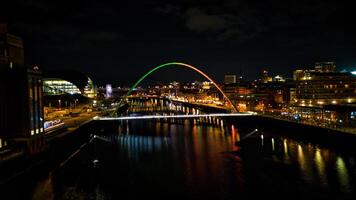 noche paisaje urbano con iluminado arco puente reflejando en agua, urbano horizonte en antecedentes en Newcastle sobre Tyne foto