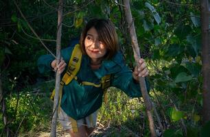 asiático mujer mochila amarillo y vistiendo chaqueta verde de viaje solo en el bosque y contento excursionismo en el bosque vacaciones viaje, estilo de vida conceptos. foto