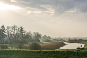 View over the Bossche Broek nature reserve with the sun breaking trough the clouds and shining trough the trees with a runner in the background. photo