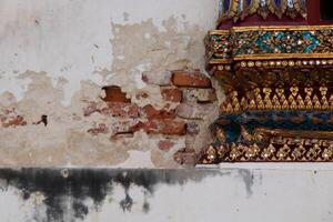 Ancient white cement wall cracked open red brick inside beside ancien native Thai art of church in temple with dirty stain on wall, Thailand. photo