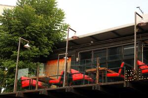 Bright red chairs and tables on large outdoor balcony of second floor wood house with glass fence. photo