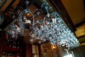 Crystal empty wine glasses hanging on the background of a bar counter. Clean wine glasses prepared by bartender and hung on the bar at a restaurant. photo