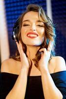 Shot of a pretty young woman in headphones with charming smile listening to music in a studio. Smiling motion female with earphones looking at camera. Close-up photo