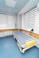 Modern comfortable bed in hospital ward. Clinical sterile room for patient health care. photo