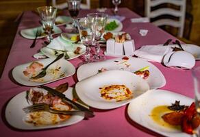 Messy table with dirty dishes after party on food table. Leftover food, empty glasses, dirty dishes on a table. photo