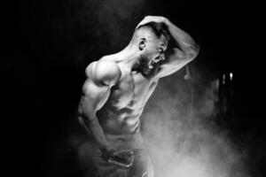 Strong brutal bodybuilder man with perfect abs, shoulders,biceps, triceps and chest showing his biceps. Scream motivation. Black and white. photo