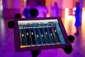 Sound and light mixer console on tablet with microphone over the blurred background. Recording mixing panel with digital mixer tablet in music studio. photo