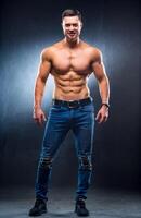 Muscular guy with naked torso posing with hands on waist. studio photo. Portrait of a handsome man in jeans. Full length photo. Closeup photo