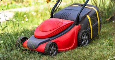 Red lawn mower with a tank for grass in green garden, backyard. Landscape, terrain concept. Closeup photo