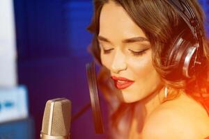 Caucasian female singer with headphones and closed eyes sings at the mic in a recording studio. Portrait of a beautiful woman in headphones singing. Closeup photo. photo