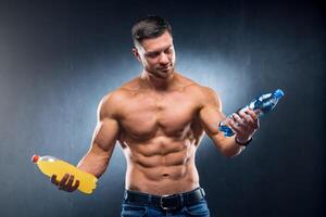 Sexy sportsman holding a bottle of water and soda. Choosing between healthy and harmful drink. Portrait. Closeup photo