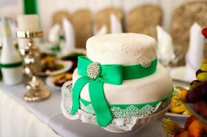 Delicious white cake in the form of a hat with green ribbon and a bow on the table background. Festive wedding table in the restaurant. Close-up photo