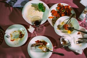 Top view dirty and empty plates and forks, wine glasses after banquet in the restaurant. Leftovers, empty plates, left half eaten food and meals. photo