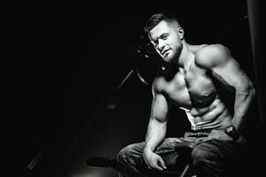 Muscular model young man on gym background. Fashion portrait of strong brutal guy with trendy hairstyle. Sexy naked torso, six pack abs. Sport workout bodybuilding concept. Black and white photo