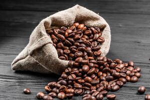 Sack full of aroma coffee beans pouring on the table. Fresh roasted arabica grains isolated on the wooden surface. Close-up photo