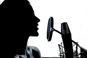 Female vocalist performing music in front of the microphone in the recording studio. Profile of a woman with mic in studio. Black and White. photo