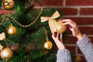 woman's hands adorn Christmas tree by golden toy with a bow-knot on the background photo