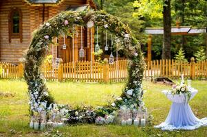 Arch for the wedding ceremony. Decorated with fabric flowers and greenery. Is located in a pine forest. Background church. Wedding decorations in rustic style. Just married. Wedding decor. photo