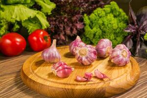 Garlic bulbs on a wooden board with a green salad in the background. Delicious vegetarian food photo