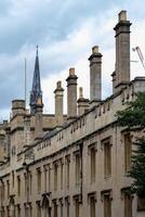 Historic building facade with chimneys and a spire in the background under a cloudy sky in Oxford, England. photo
