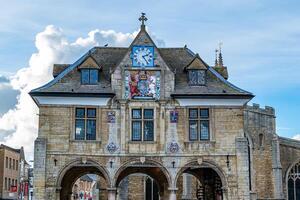 Old stone building with arches and a clock under a cloudy sky in Peterborough, England. photo