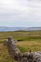 Rustic stone wall leading through a tranquil, rolling countryside under a cloudy sky in Peak District, England. photo