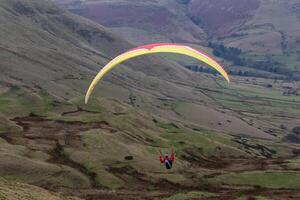 Paraglider soaring over scenic green hills with a colorful canopy against a muted sky in Peak District, England. photo