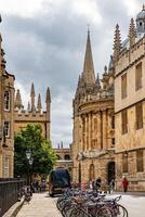 Historic Oxford street scene with bicycles, pedestrians, and Gothic architecture under a cloudy sky. photo