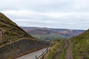 Scenic view of a winding road along a hilly landscape with overcast skies in Peak District, England. photo