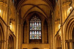 Interior of a Gothic cathedral showcasing an ornate stained glass window with arches and warm ambient lighting in Peterborough, England. photo