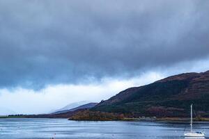 Sailboat on a calm lake with overcast skies and autumn hills in the background in Scotland. photo