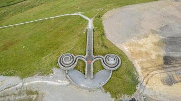 Aerial view of a unique triple-spiral design on the ground, with pathways leading to it amidst a grassy landscape. photo