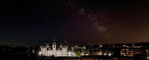 panorámico noche horizonte con iluminado edificios debajo un estrellado cielo presentando el lechoso camino en Edimburgo, Escocia. foto