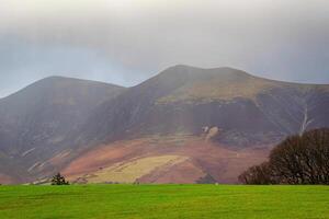 Rolling green hills with misty mountain backdrop under overcast sky. photo