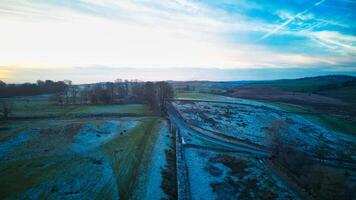 Aerial view of a countryside road at dawn with fields and trees under a soft blue sky with wispy clouds. photo