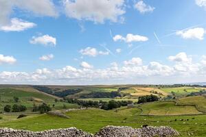 Idyllic rural landscape with rolling hills, stone walls, and a clear blue sky with wispy clouds. photo