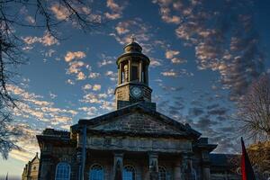 Historic stone building with clock tower against a dramatic sky at sunset in Lancaster. photo