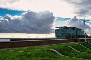 Modern building against a dramatic sky with sunbeams, green grass in the foreground and wavy landscape design. photo