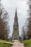 Gothic church with spire surrounded by trees under a cloudy sky. photo