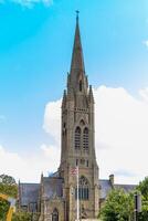 Gothic church spire against a blue sky with clouds, surrounded by greenery in Bath, England. photo