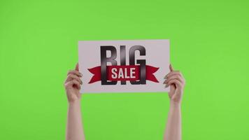 Big Sale advertisement inscription on paper sheet in womans hands on chroma key. Slow motion video